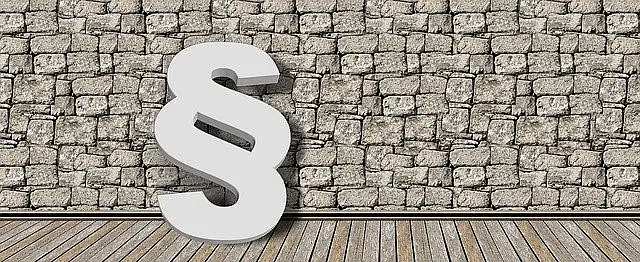 Ein weißes Paragrafen-Zeichen lehnt an einer Steinwand